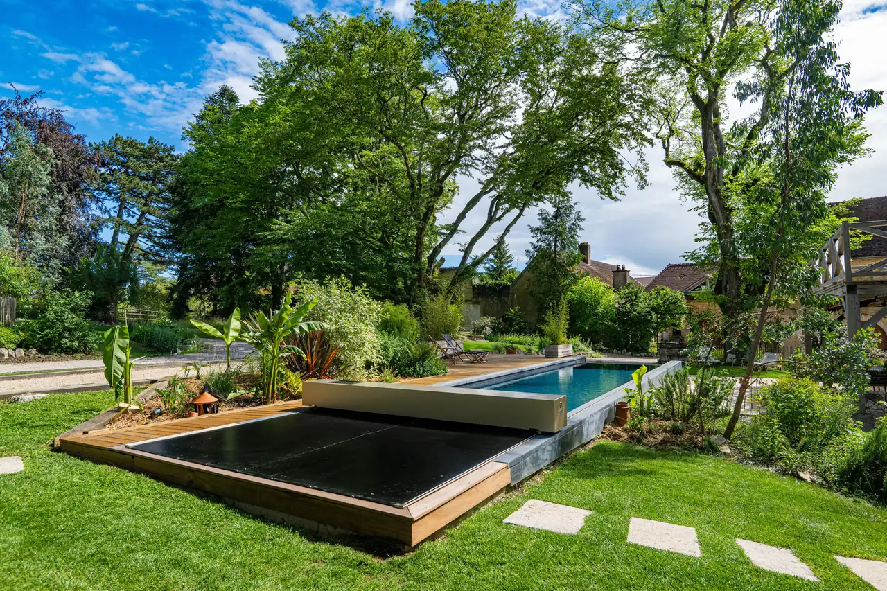 Piscine extérieure partiellement recouverte d’une membrane Coverseal noire, intégrée à un jardin verdoyant avec terrasse en bois.